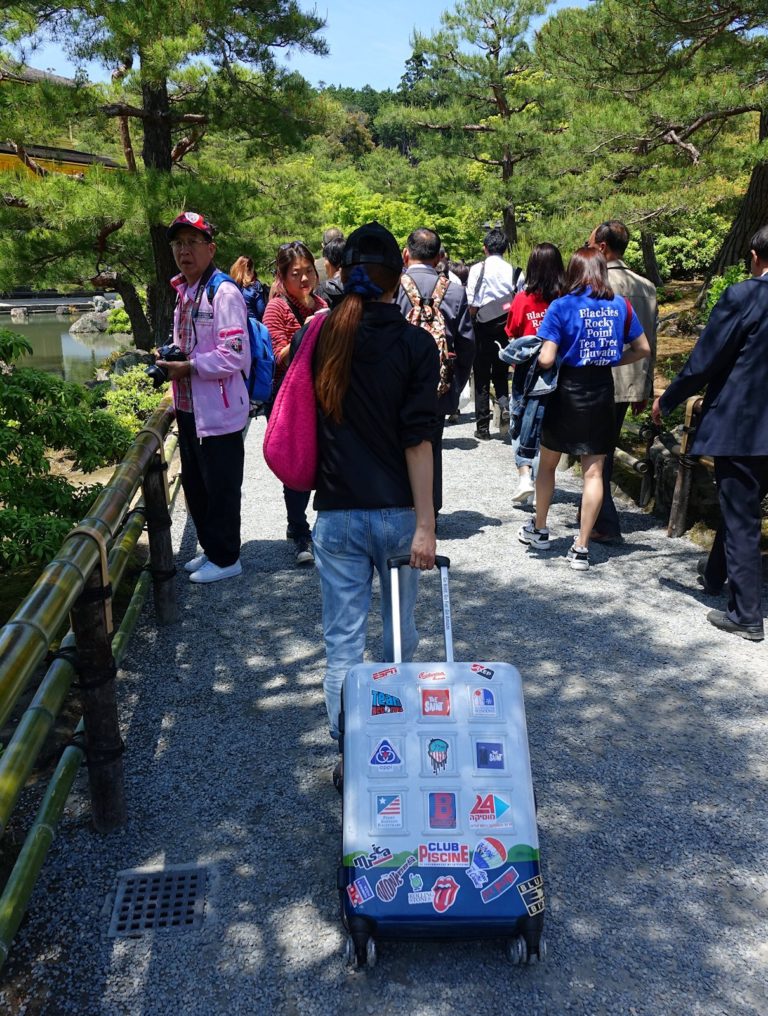 Tourist with hand luggage at Kinkaku-ji Golden Pagoda in Kyoto, Japan.