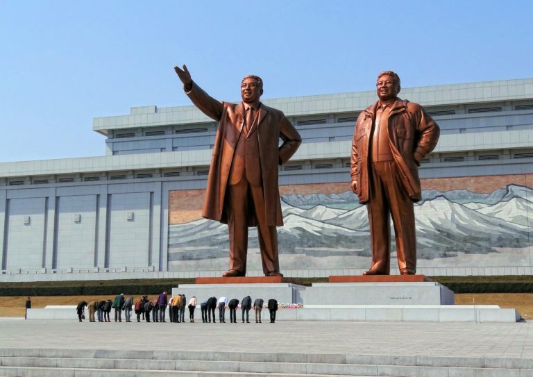 Photo of a group of tourists bowing in front of Kim statues in Pyongyang, North Korea.