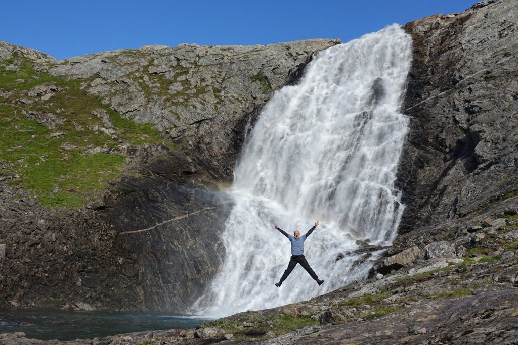 Photo of man jumping in front of a waterfall with no name in Northern Norway.