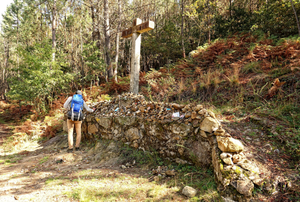 Photo of Santiago pilgrim leaving a small rock at the stone cross beyond Labruja hill on Caminho Portugues.