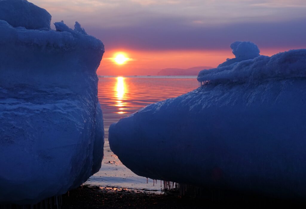 Photo of sun setting between two large pieces of ice